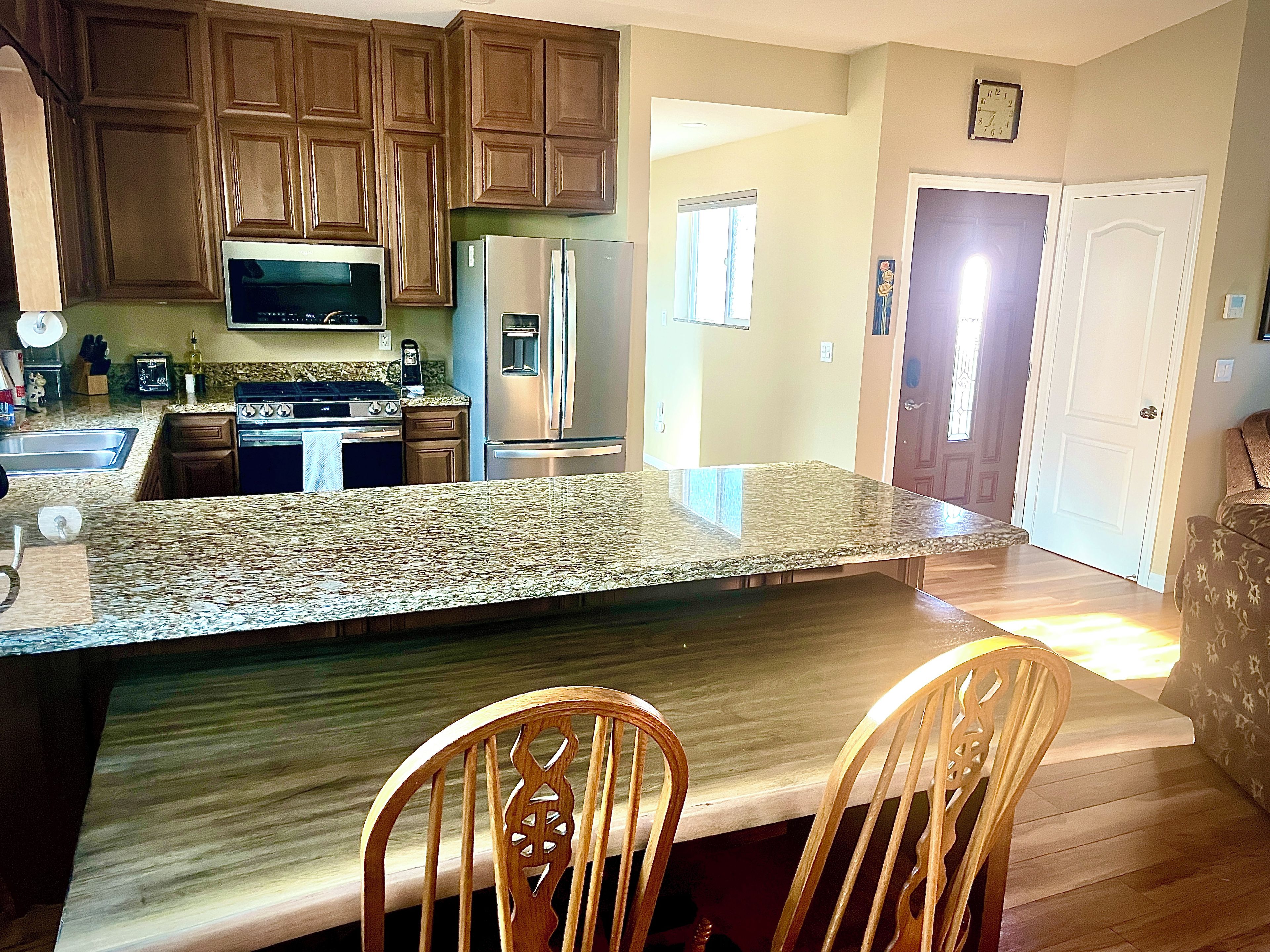 A kitchen with granite countertops, wooden cabinets, stainless steel appliances, and a dining area with two wooden chairs.