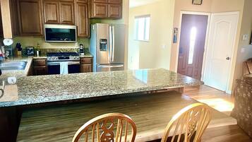 A kitchen with granite countertops, wooden cabinets, stainless steel appliances, and a dining area with two wooden chairs.