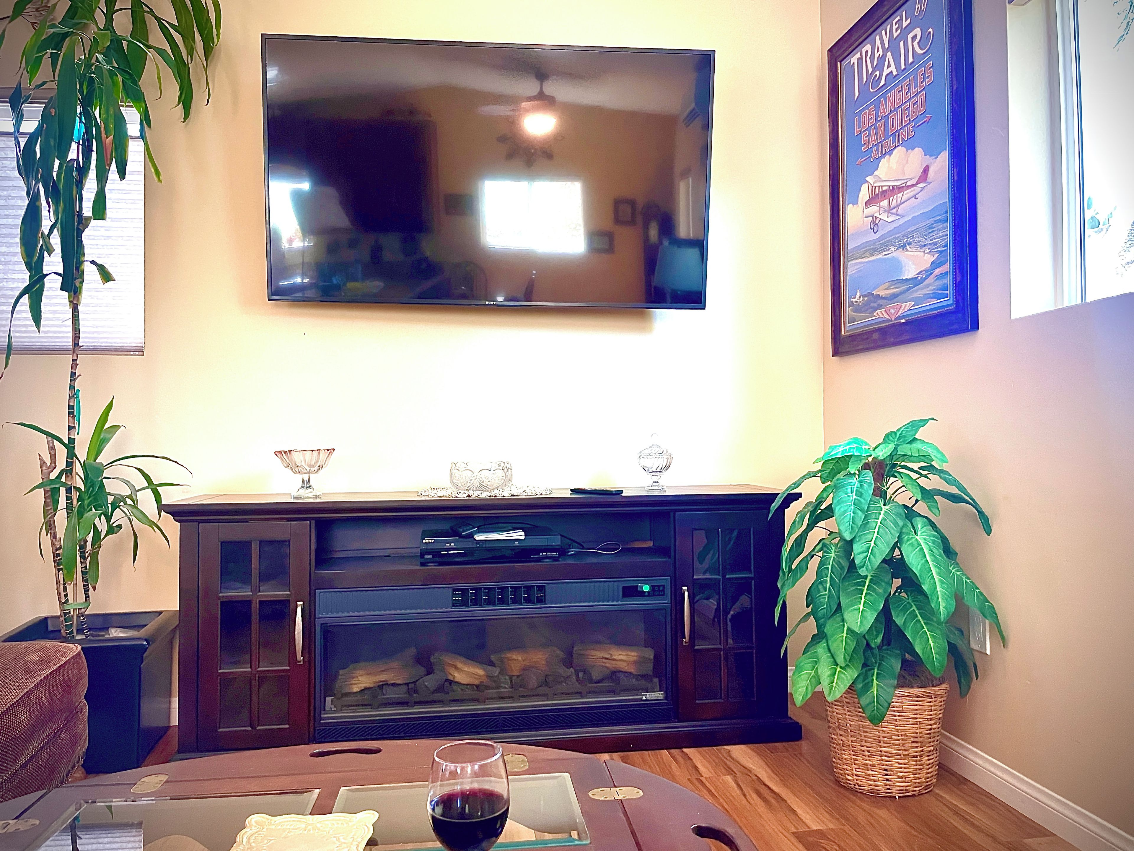 Un salon doté d’un téléviseur à écran plat fixé au mur, d’une cheminée avec une porte en verre et d’une table à manger sur laquelle se trouve un verre de vin rouge.
