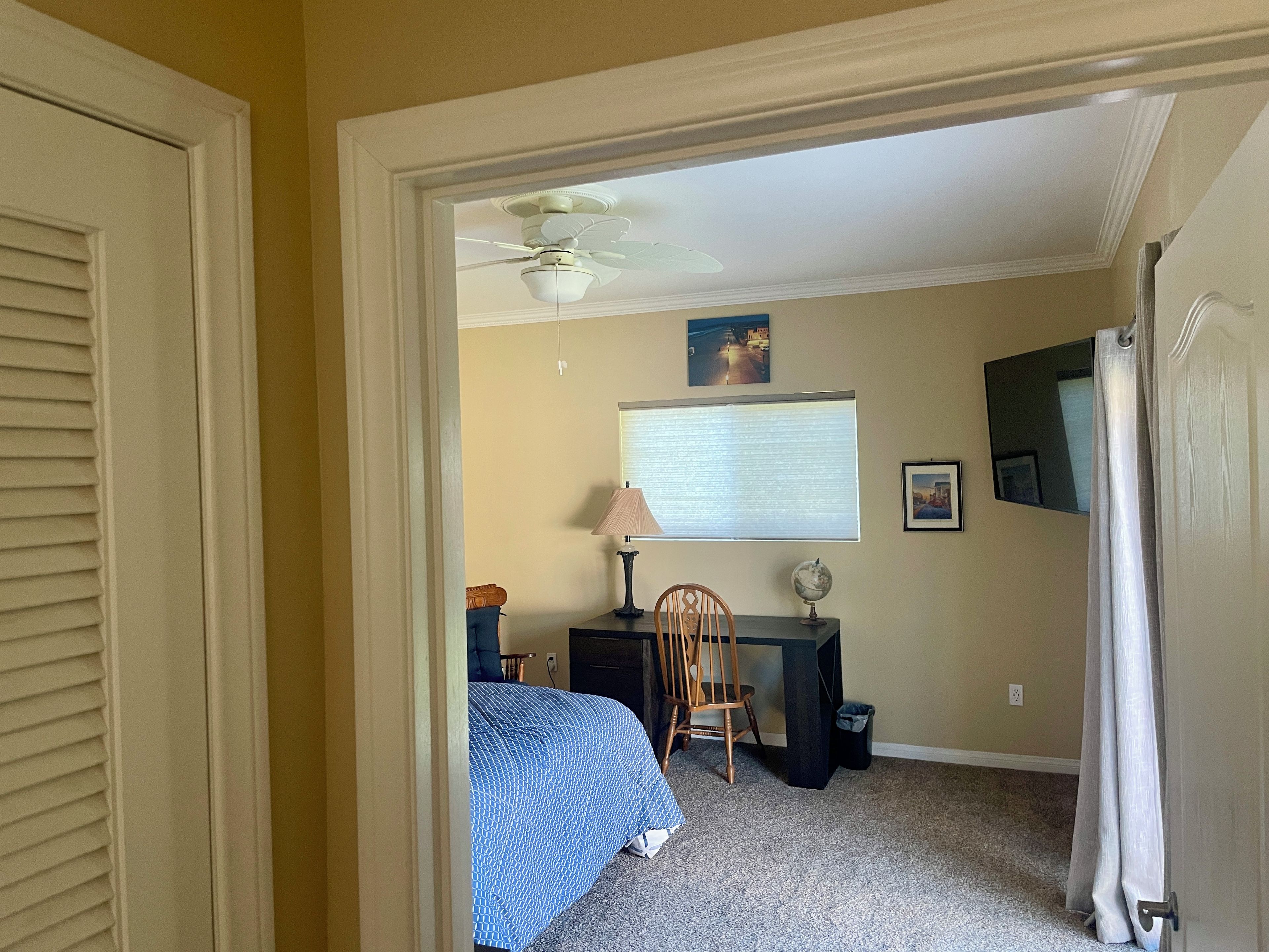 Une chambre à coucher avec un lit, un bureau, une chaise, un globe terrestre et un ventilateur de plafond.