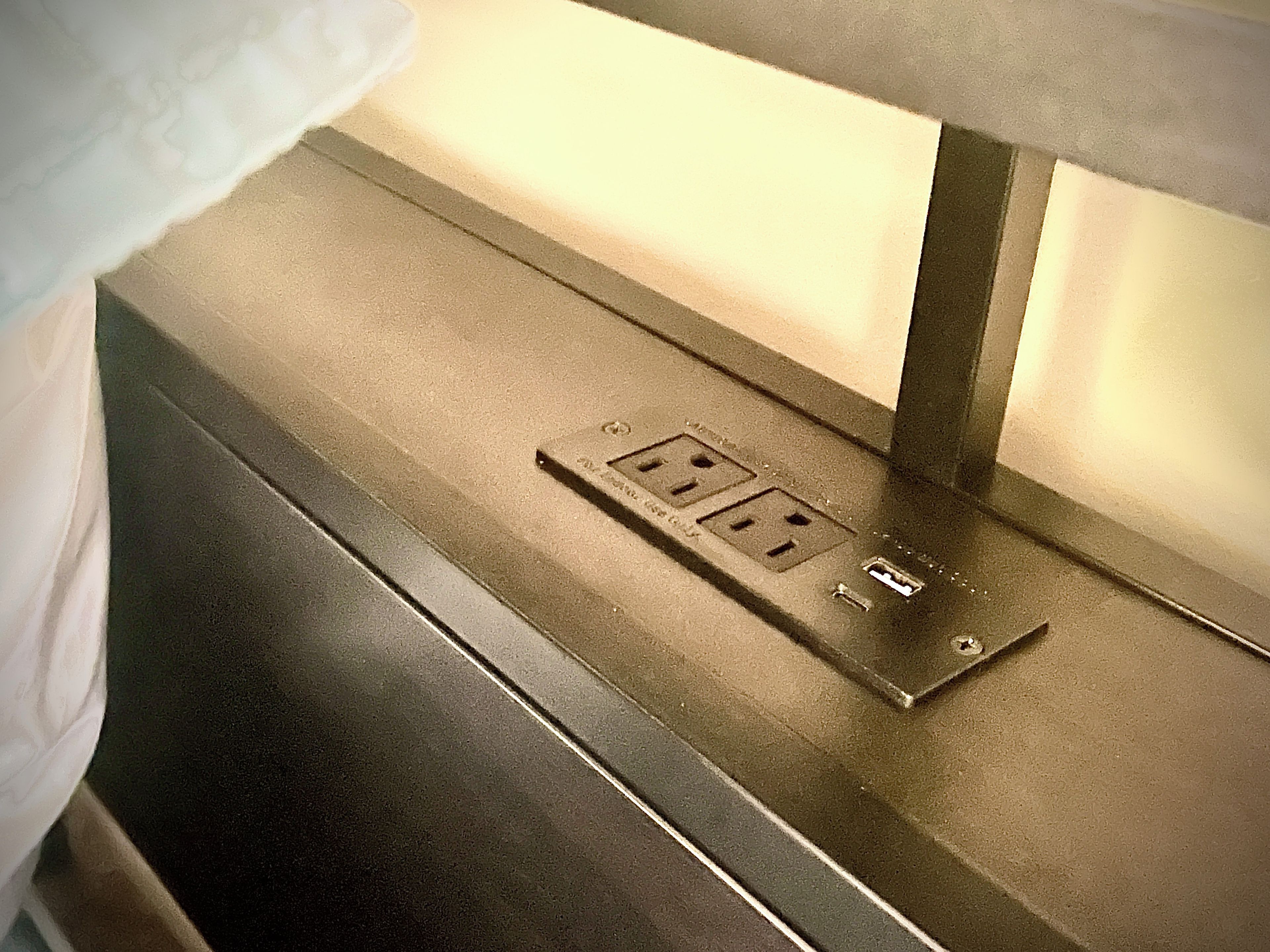 A close-up of a power outlet on a metallic surface, likely part of a room's interior.
