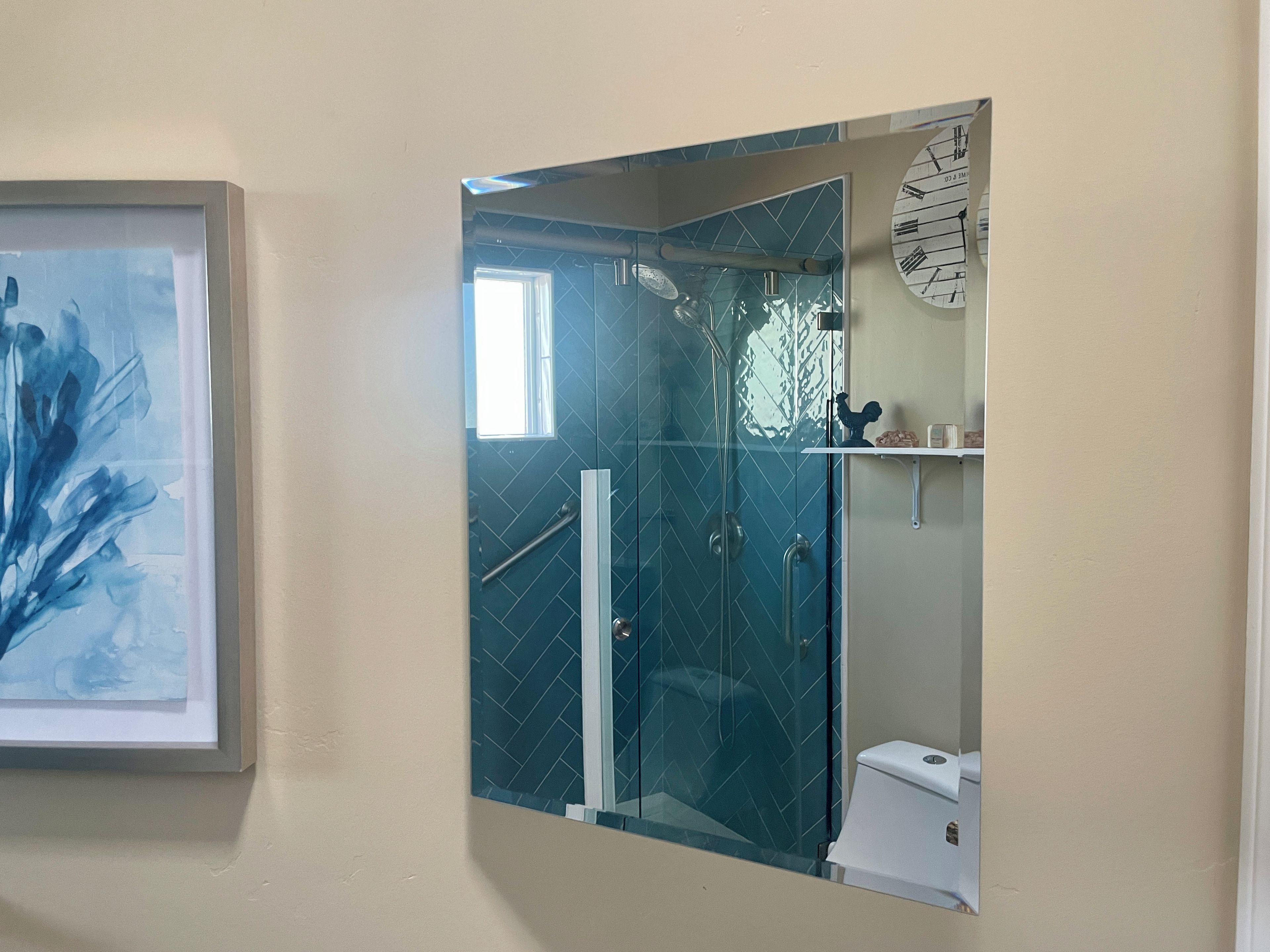 A bathroom with a glass shower enclosure, a white toilet, and a framed abstract painting on the wall.