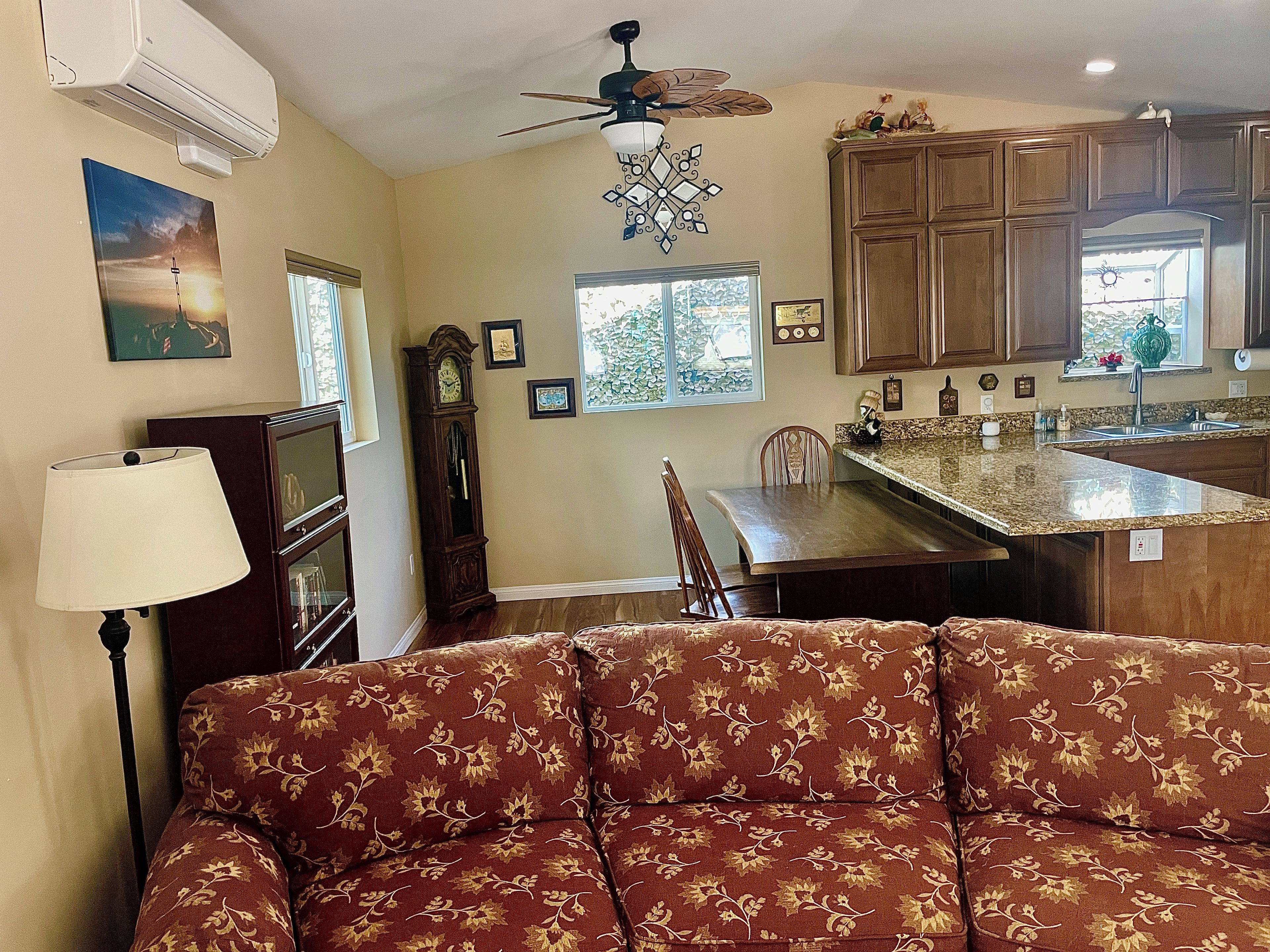 A living room with a sofa, a dining table, and a kitchen area with cabinets and a window.
