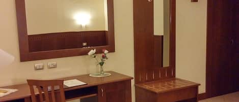 A hotel room with a wooden desk, a chair, a television mounted on a stand, and a large mirror.