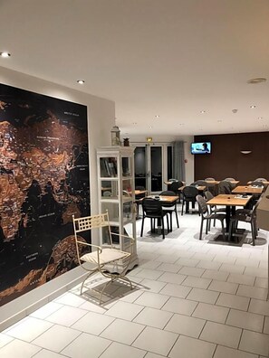 Un comedor moderno con mesas y sillas, un mapa grande en la pared y una pantalla de televisión.