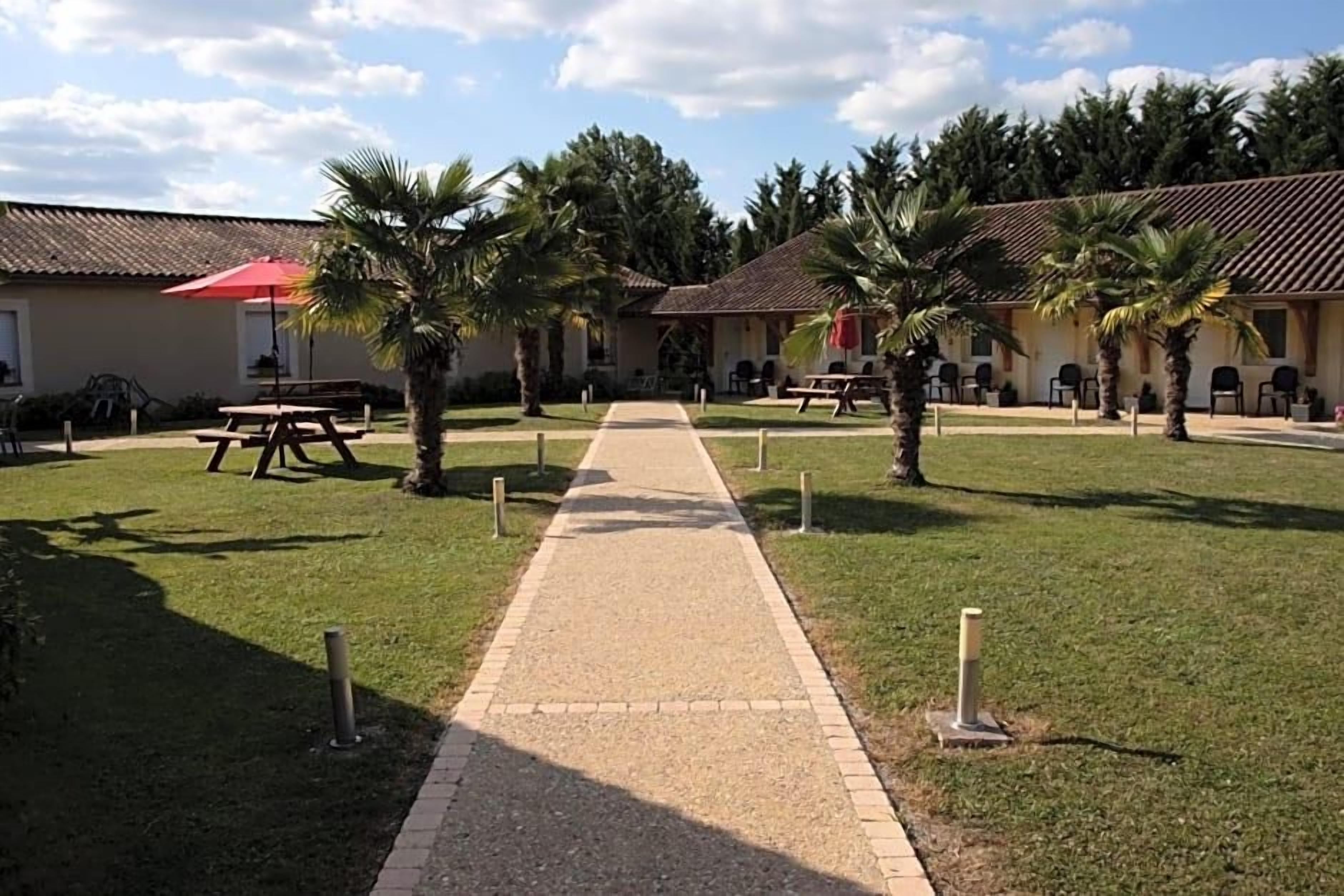 Un chemin menant à un bâtiment doté d’une terrasse et bordé de palmiers.