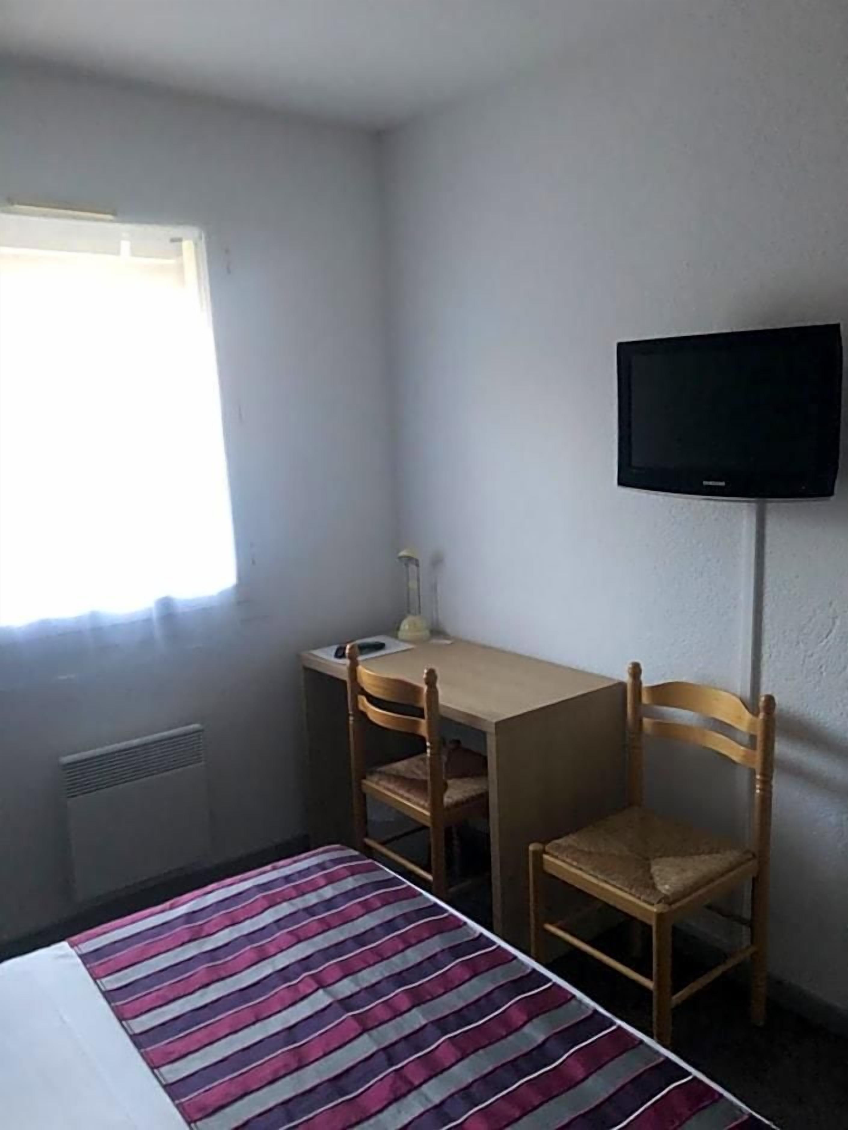 A small room with a bed, a desk, two chairs, a television, and a window.