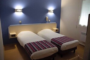Habitación de hotel con dos camas, cada una con colcha a rayas, cabecero blanco y mesitas de noche fijadas a la pared.