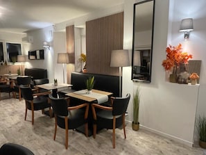 Uma área de refeições moderna com um sofá preto, cadeiras de madeira e uma mesa com um vaso de flores.