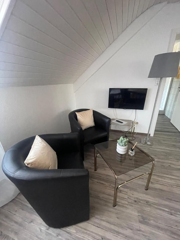 Uma sala de estar moderna com um sofá preto curvo, uma TV de tela plana e uma mesa de centro de vidro.