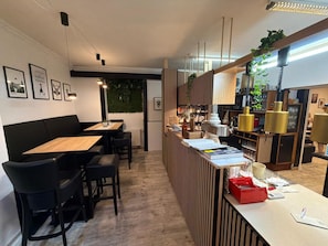 Interior moderno com mesa de jantar de madeira, cadeiras pretas, área de bar com balcão e planta suspensa na parede.
