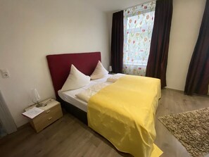 Un dormitorio con una cama, una mesita de noche, una ventana con cortinas y suelo de madera.