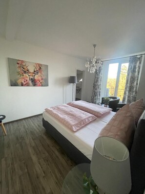 Un dormitorio con cama, una araña, un cuadro y una ventana con cortinas.
