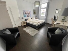 A modern bedroom with a bed, bedside tables, a desk, and two armchairs.