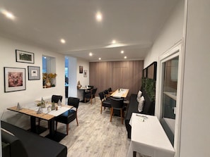 Uma área de jantar moderna com mesa de madeira, cadeiras pretas e parede listrada ao fundo.