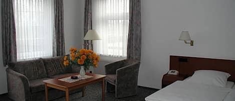 Habitación de hotel con cama, sofá, una mesa con un jarrón de flores, una lámpara y una mesita de noche.