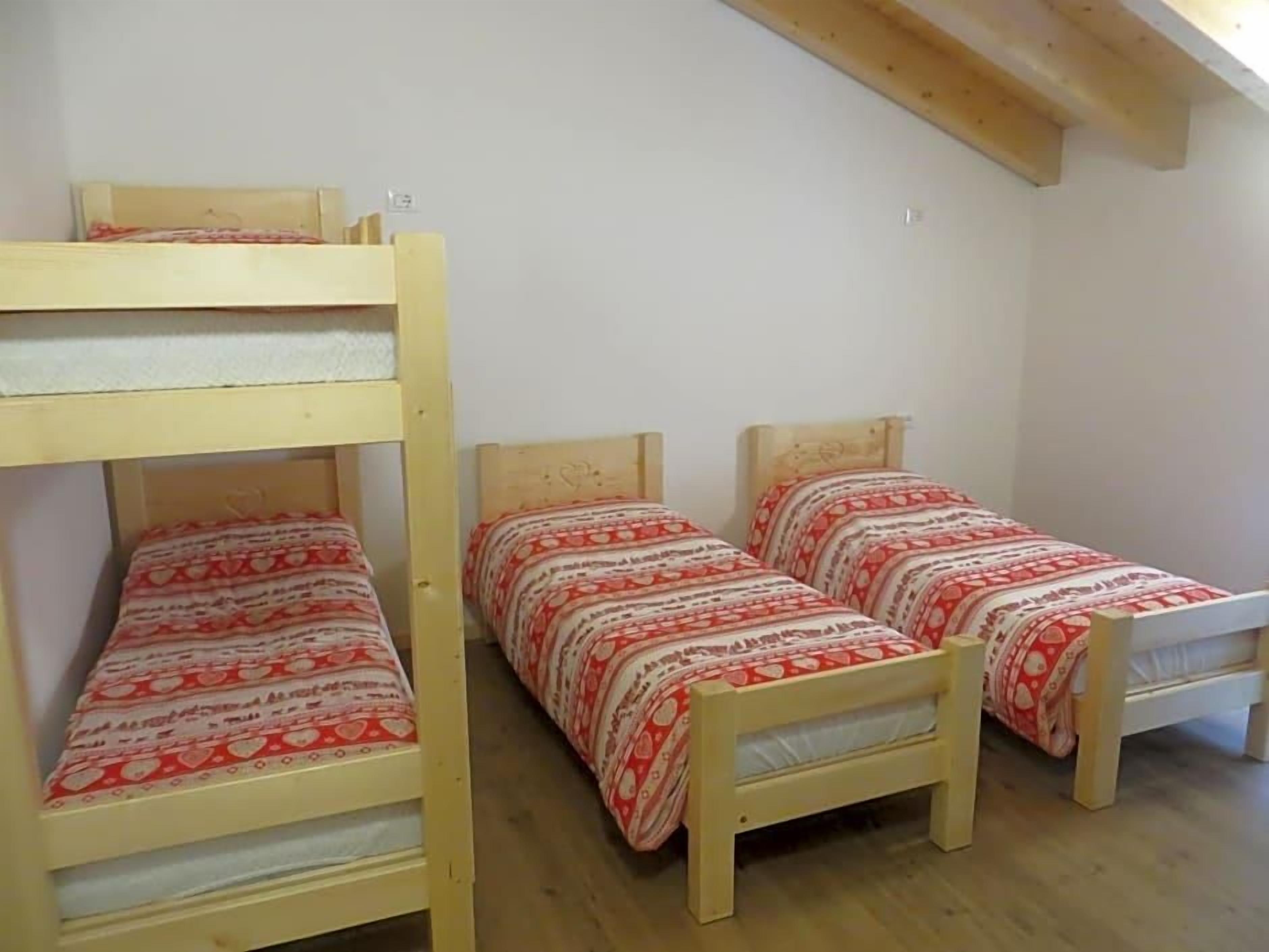 A dormitory room with two bunk beds and two single beds, wooden flooring, and white walls.