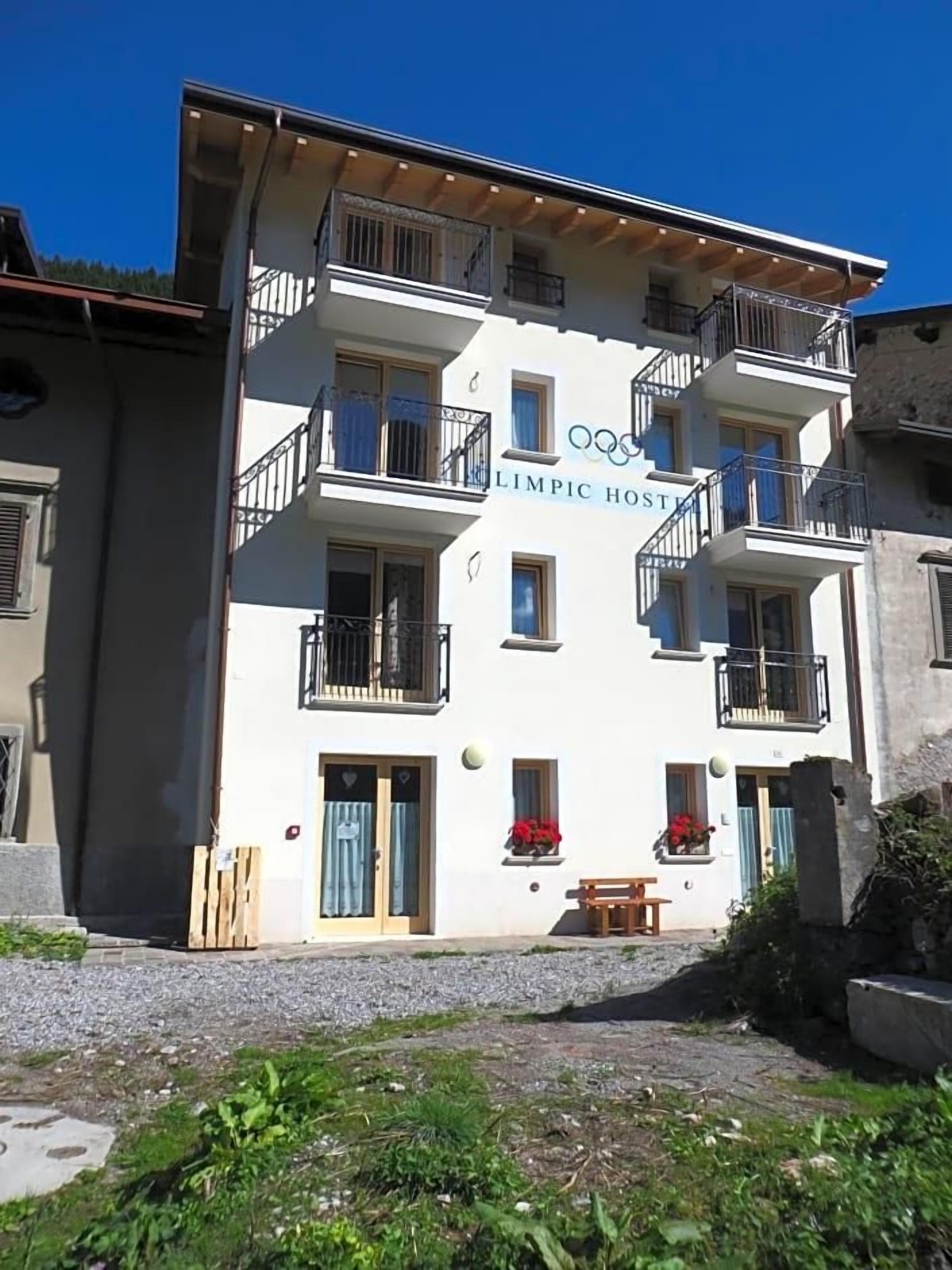 A multi-story building with balconies, a sign indicating it is a 'LIMPIC HOSTEL,' and a small outdoor seating area.