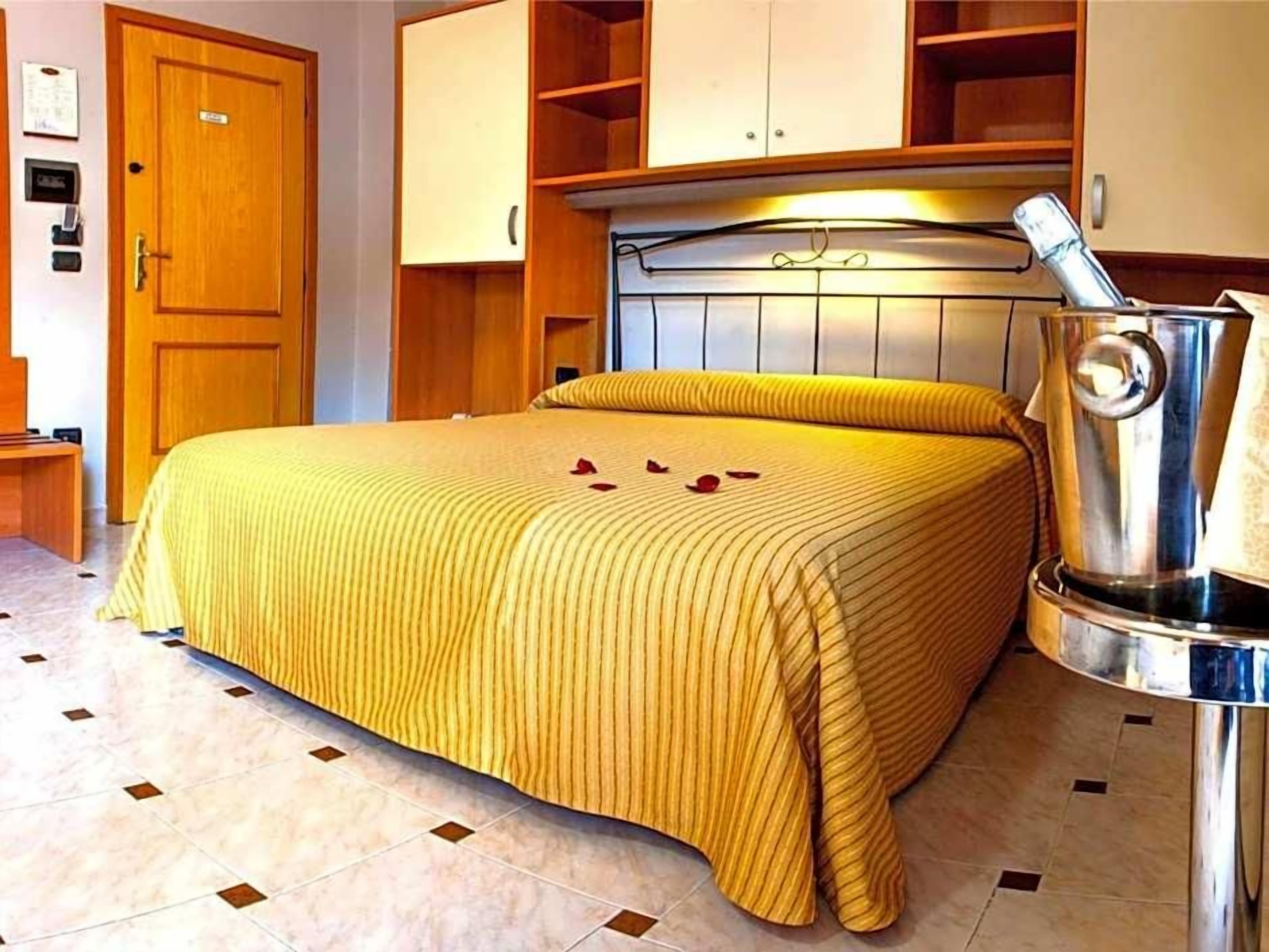 A hotel room with a bed, a wooden door, a minibar, and a tiled floor.