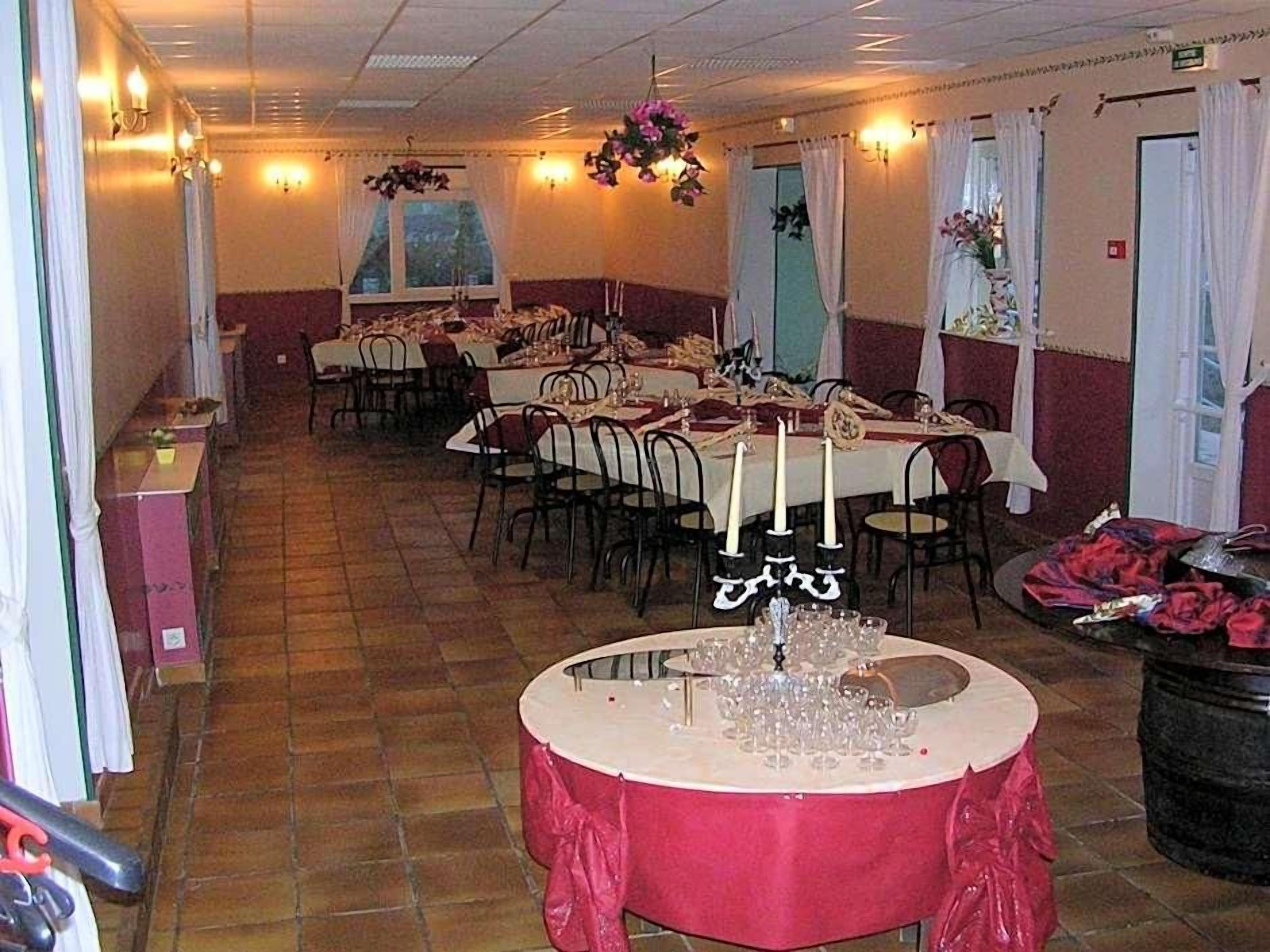 A banquet hall with multiple round tables set for dining, each with white tablecloths and candle centerpieces.