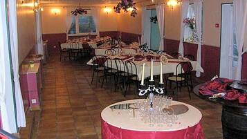 A banquet hall with multiple round tables set for dining, each with white tablecloths and candle centerpieces.