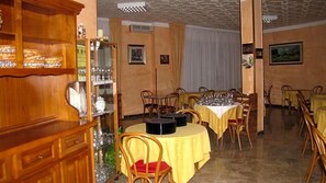 A dining area with round tables covered with yellow tablecloths, wooden chairs, and a buffet area with glassware and dishes. - Albergo La Primula (Chianciano Terme)