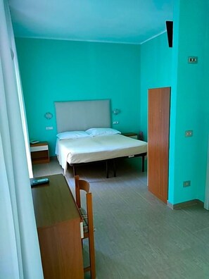A small, single-bed room with a wooden desk and chair, a wardrobe, and a bedside table. - Albergo La Primula (Chianciano Terme)