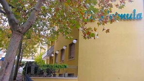 A building with a yellow facade, a sign with the word 'Formula,' and a tree with autumn leaves in the foreground. - Albergo La Primula (Chianciano Terme)