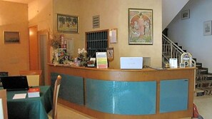 A reception desk with a laptop, a framed picture, and a staircase in the background. - Albergo La Primula (Chianciano Terme)