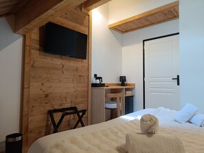 Un dormitorio con cama, televisor montado en una pared de madera, escritorio con silla y una puerta.