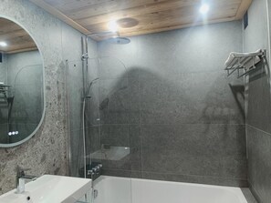 Un baño moderno con ducha envuelta en vidrio, una bañera blanca y un espejo redondo.