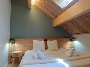 A bedroom with a sloped ceiling, a bed with white bedding, two bedside lamps, and a small wooden stool. - Hv Tel Mont Thabor Serre Chevalier (La Salle-les-Alpes)
