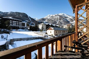 Un balcon en bois offrant une vue sur un paysage enneigé, des bâtiments et des montagnes en arrière-plan.