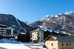 Un hôtel à plusieurs étages, une piste de ski en arrière-plan et des montagnes enneigées.