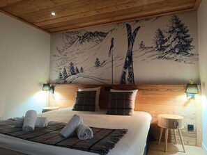 Un dormitorio con cama, dos almohadas, una colcha, una mesita de noche, una lámpara y un mural en la pared.