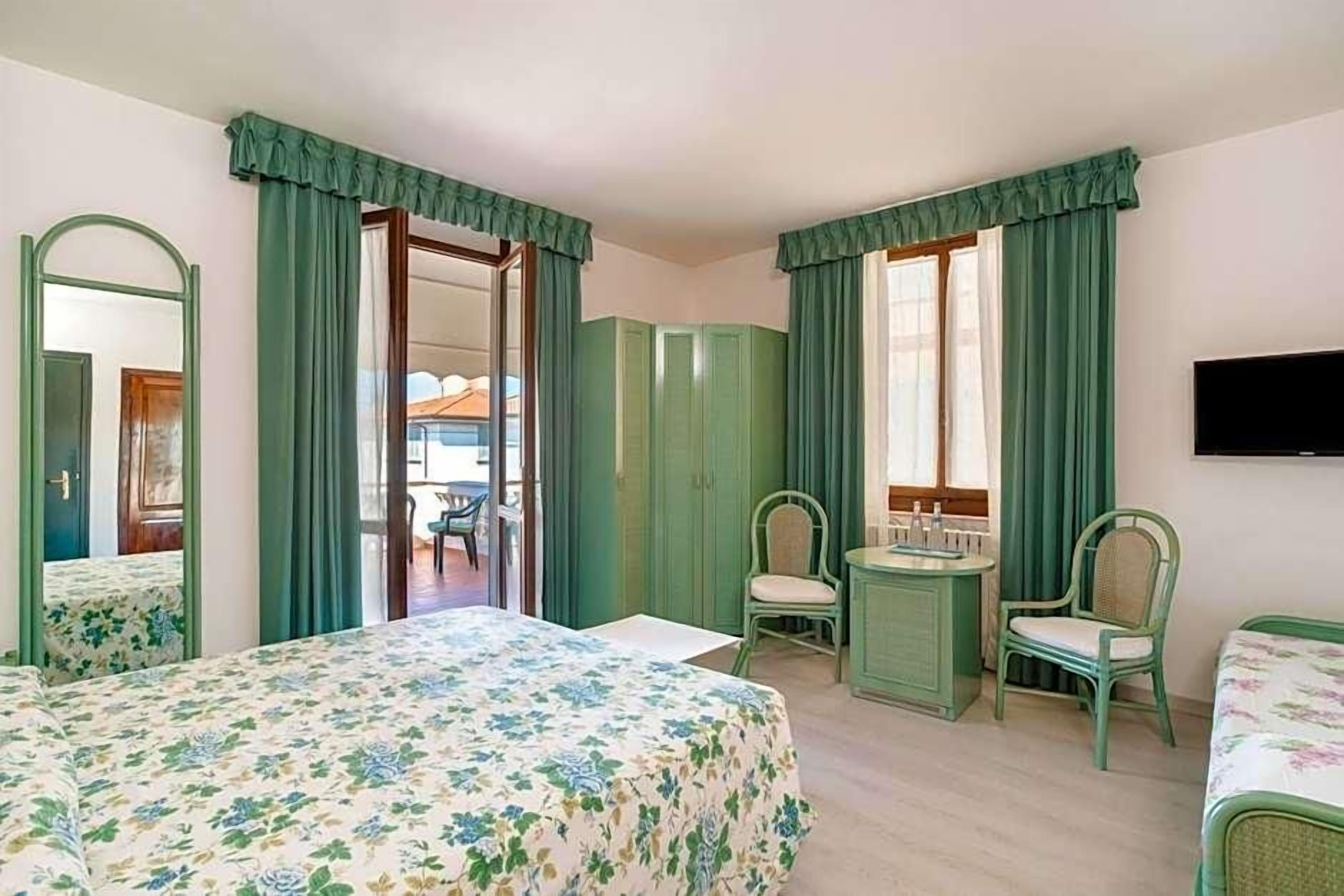 Ein Hotelzimmer mit einem Bett, zwei Sesseln, einem kleinen Tisch, einem Spiegel und einem Fernseher.