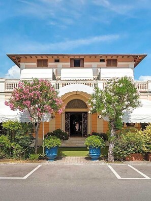 A hotel entrance with a covered driveway, an arched doorway, and potted plants. - Hotel Sonia (Forte dei Marmi)