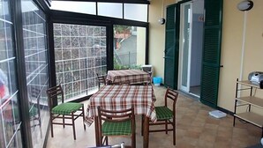 A sunlit patio with a table and chairs, a sliding door, and a view of the outside. - Hotel Adriana (Laigueglia)