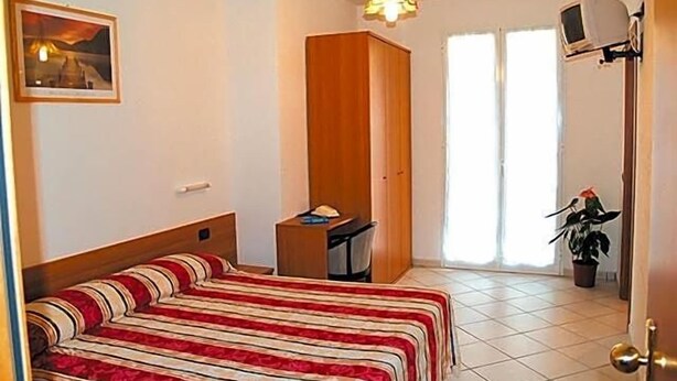 A bedroom with a bed, a desk, a chair, a television, and a window. - Hotel Adriana (Laigueglia)