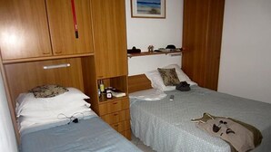 A bedroom with two beds, wooden wardrobes, a bedside table with a lamp, and a framed picture on the wall. - Hotel Adriana (Laigueglia)