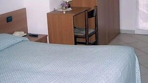 A hotel room with a bed, a desk with a chair, a wardrobe, and a window with curtains. - Hotel Adriana (Laigueglia)