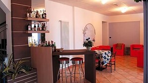 A bar area with stools, a counter with bottles, and a red sofa in a room with tiled flooring. - Hotel Adriana (Laigueglia)