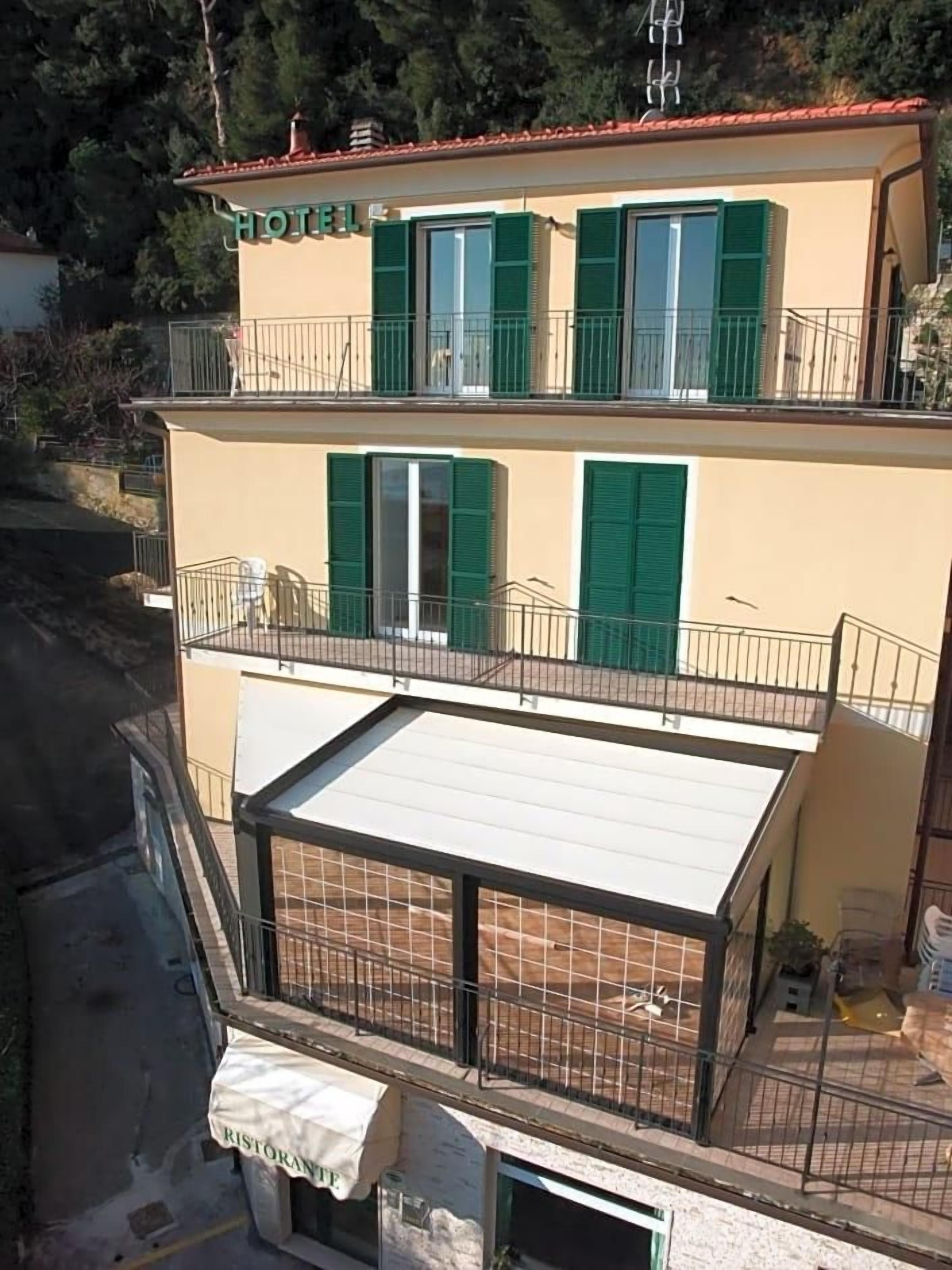 A hotel with a flat roof, green shutters, and a balcony.