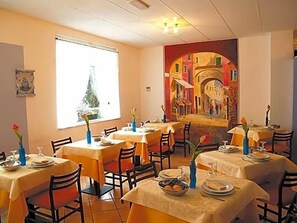 A restaurant with multiple tables, chairs, and a large window. - Hotel Adriana (Laigueglia)