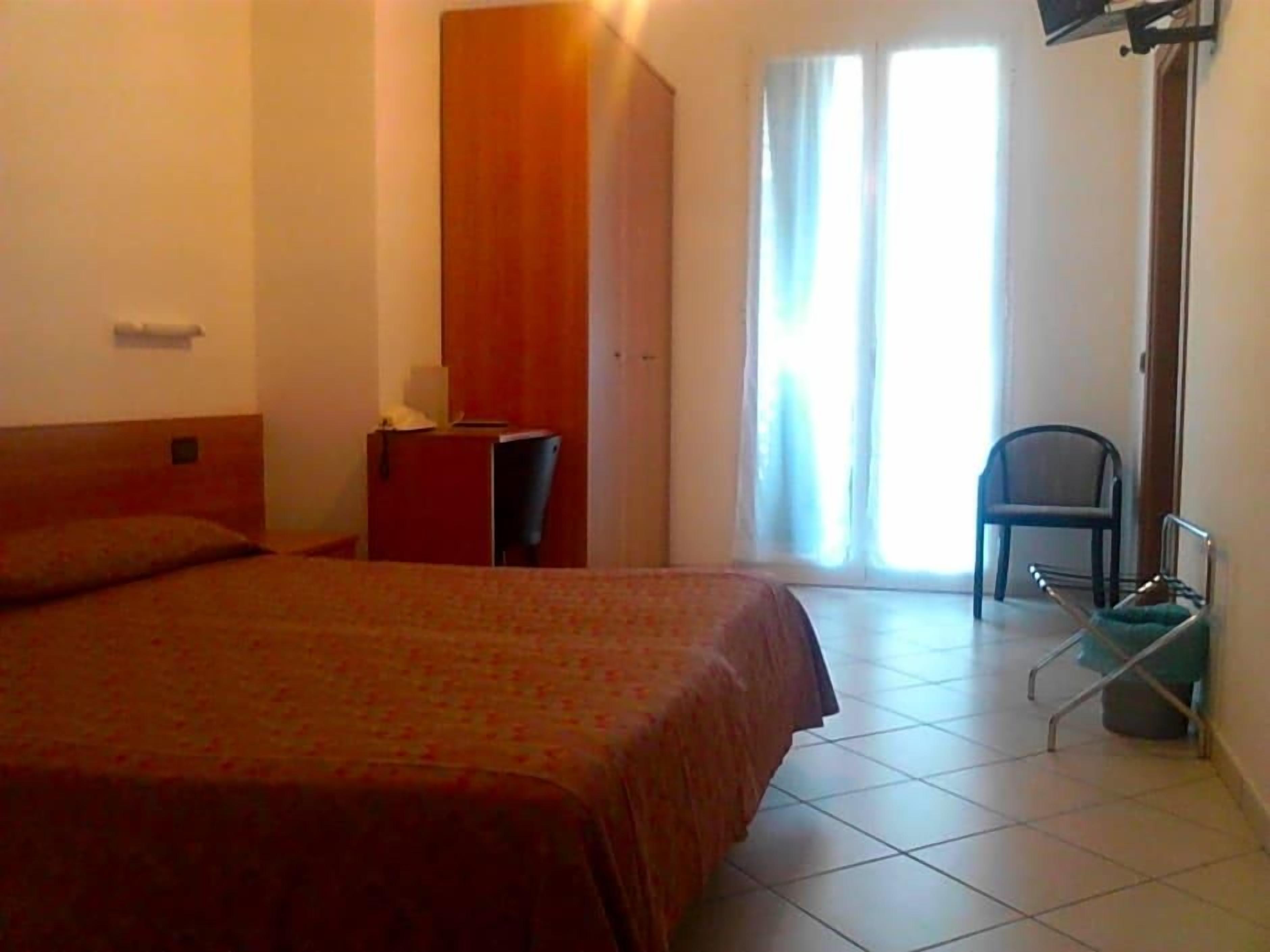 A bedroom with a bed, a desk, a chair, and a wheelchair.