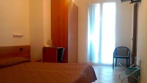A bedroom with a bed, a desk, a chair, and a wheelchair. - Hotel Adriana (Laigueglia)