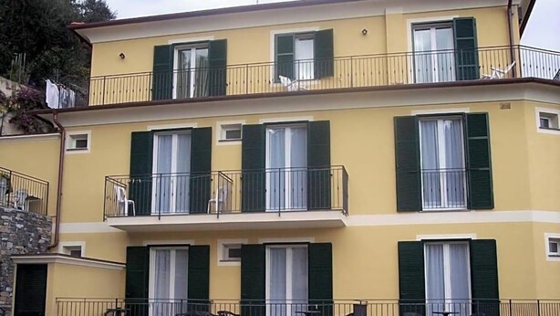 A multi-story building with balconies, windows with shutters, and outdoor furniture. - Hotel Adriana (Laigueglia)