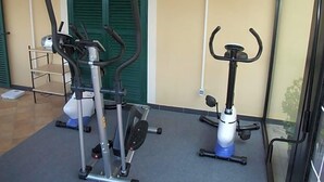 A gym with stationary bikes and a treadmill, a small table, and a chair. - Hotel Adriana (Laigueglia)