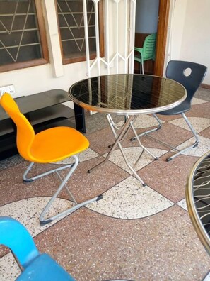 A round glass table with metal legs, two orange chairs, and a blue chair. - Larosa Executive Guest House (Kumasi)