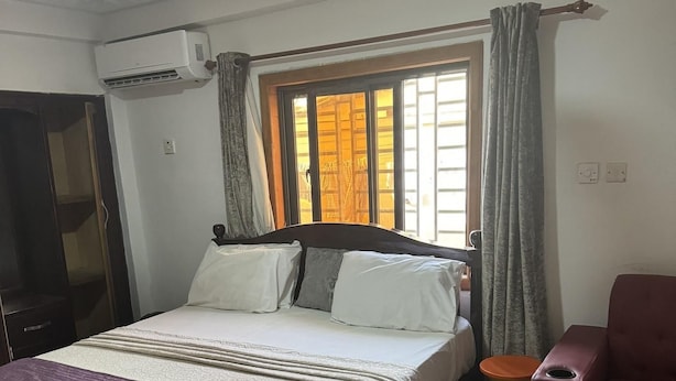 A bedroom with a bed, a chair, a window with curtains, and a ceiling fan. - Larosa Executive Guest House (Kumasi)